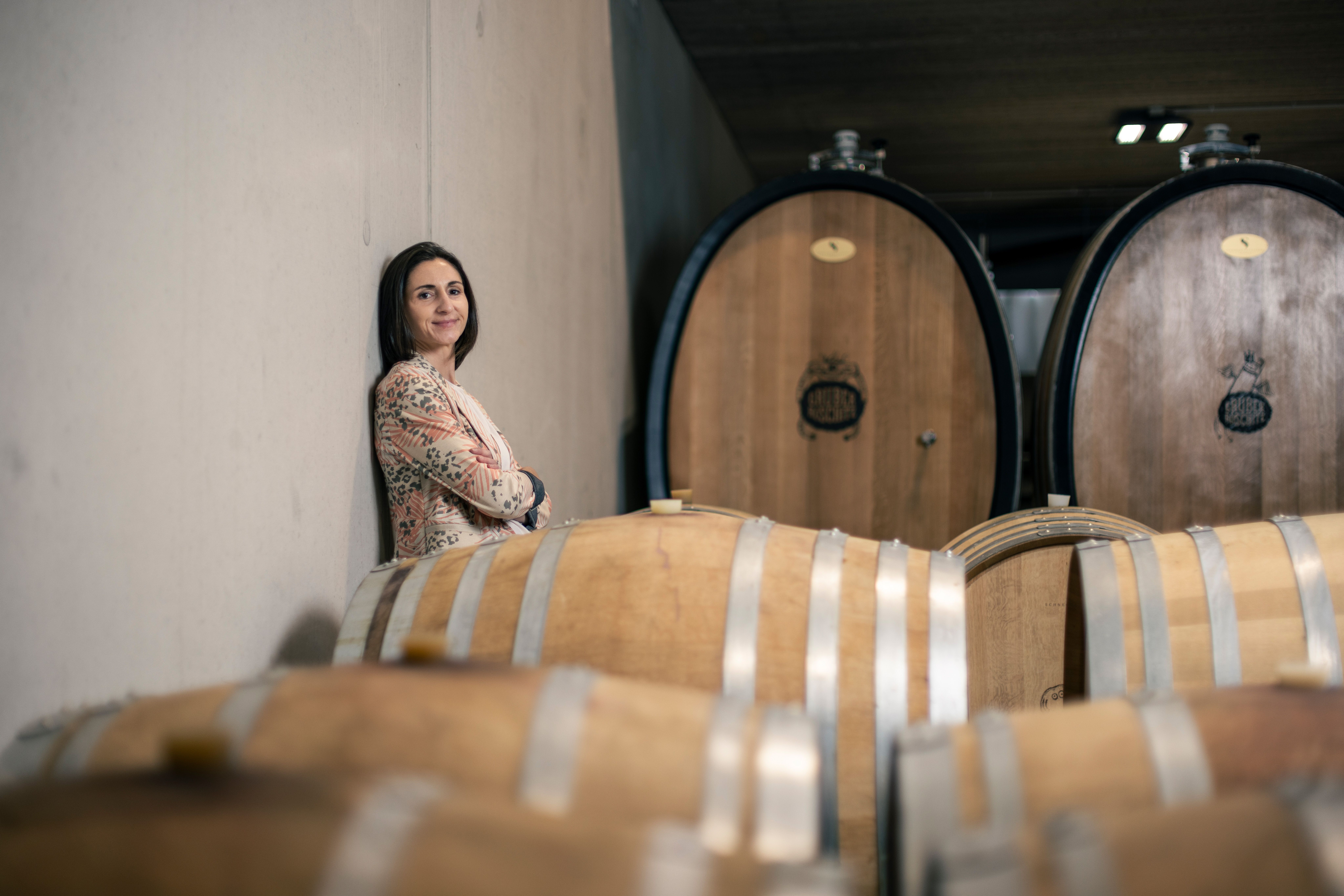 Žena opretá o stenu vo vínnej pivnici s drevenými sudmi.