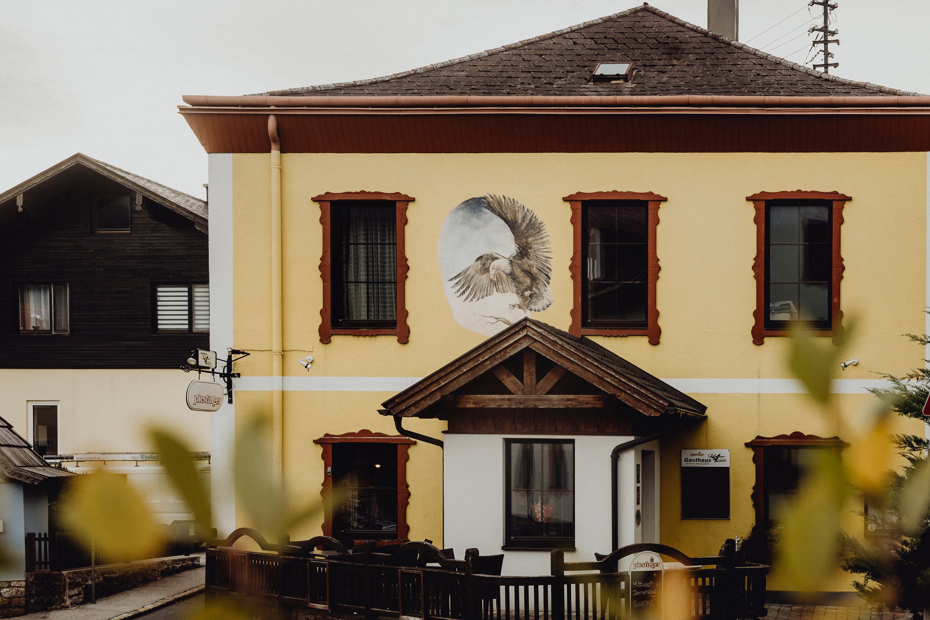 Žltá budova s nástennou maľbou orla a červenými okennými rámami.