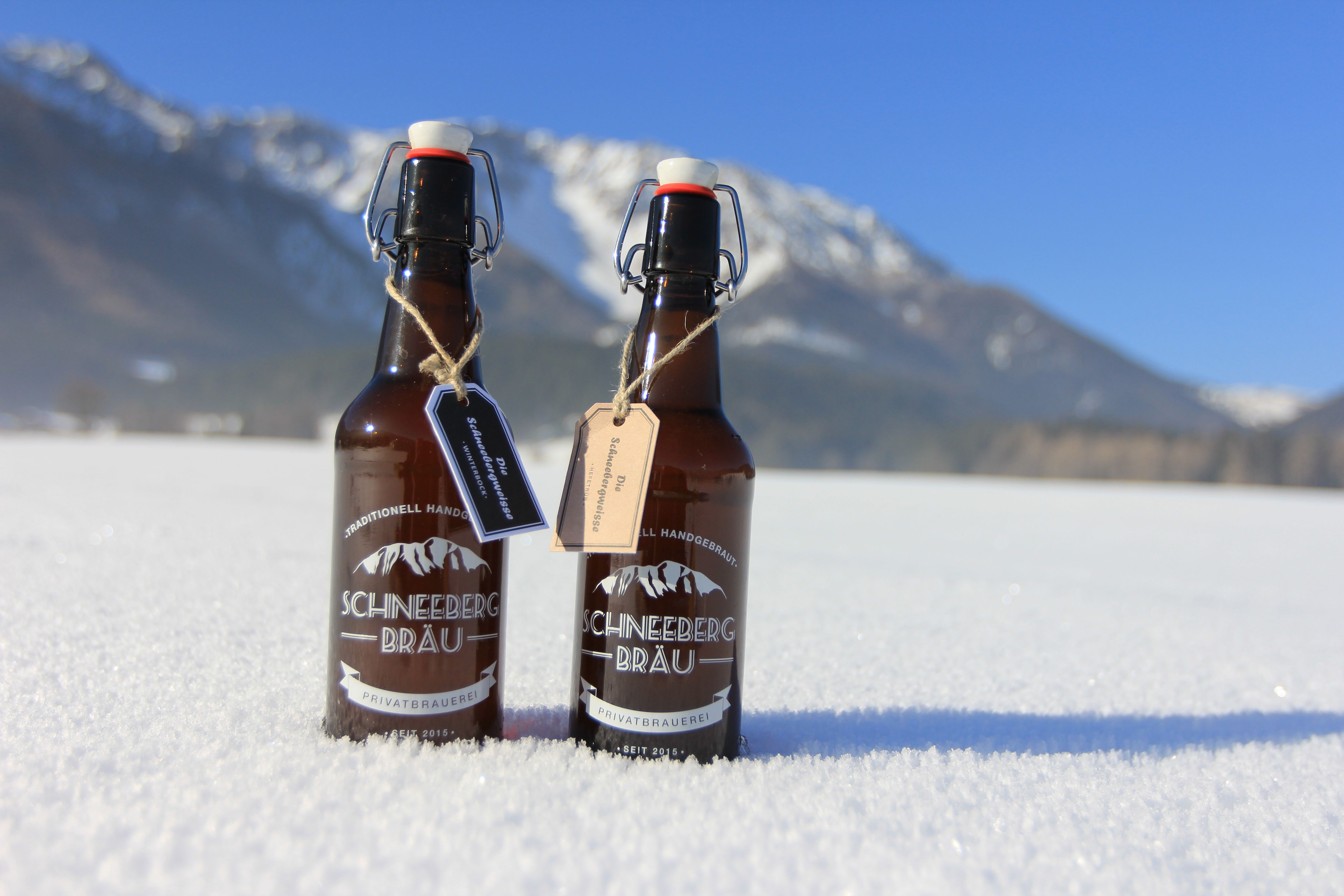 Dve fľaše piva Schneeberg Bräu stoja na snehu na pozadí hôr.