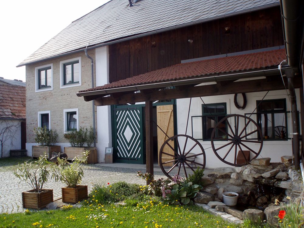 Tradičná budova s drevenou strechou a ozdobnými kolesami voza na nádvorí.