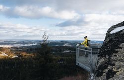 Ein Wanderer genießt die atemberaubende Aussicht auf die verschneiten Wälder und sanften Hügel, die sich bis zum Horizont erstrecken. Die frische, klare Winterluft und die ruhige Atmosphäre laden dazu ein, die Schönheit der Natur in vollen Zügen zu erleben.