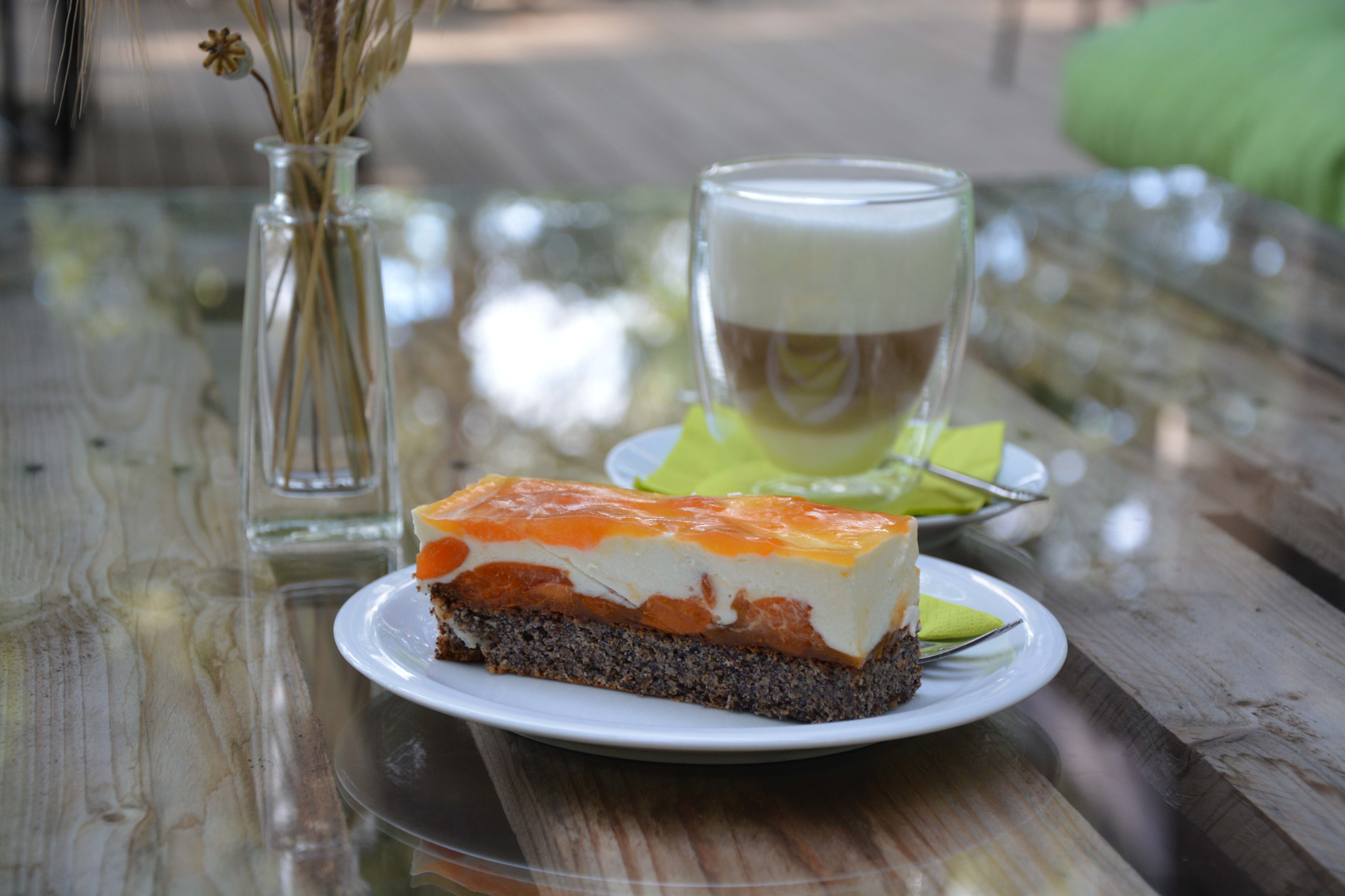 Tanier s ovocným koláčom na drevenom stole, v pozadí pohár s kávou a váza.