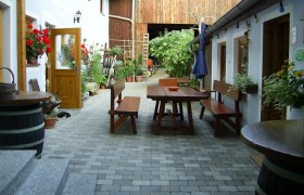 Vn&uacute;torn&yacute; dvor farmy s dreven&yacute;mi stolmi a lavicami, obklopen&yacute; rastlinami a kvetmi.