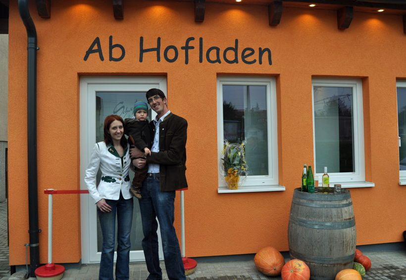 Rodina pred farmárskym obchodom Schäfer v Maria Ellend, vyzdobeným tekvicami a sudom na víno.