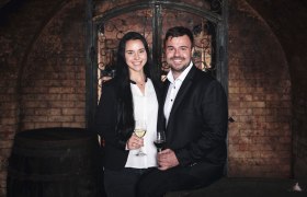 Muž a žena v elegantnom oblečen&iacute; držia poh&aacute;re na v&iacute;no vo v&iacute;nnej pivnici.