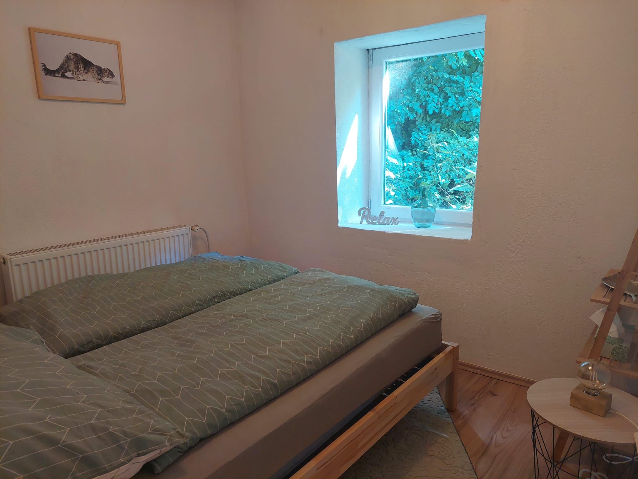 Útulná spálňa s posteľou, oknom s výhľadom na zeleň a obrazom na stene.