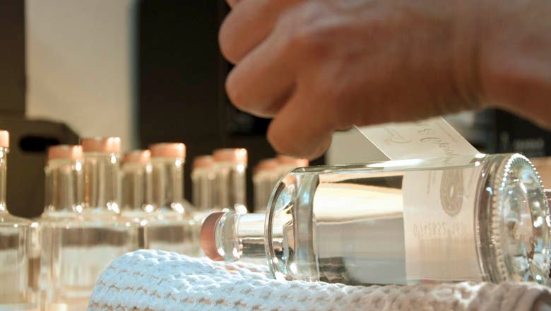 Detailný záber na ruku, ktorá lepí etiketu na fľašu brandy.