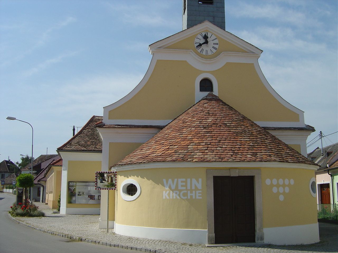 Žltý kostol s vežovými hodinami a nápisom "Weinkirche" v obci.