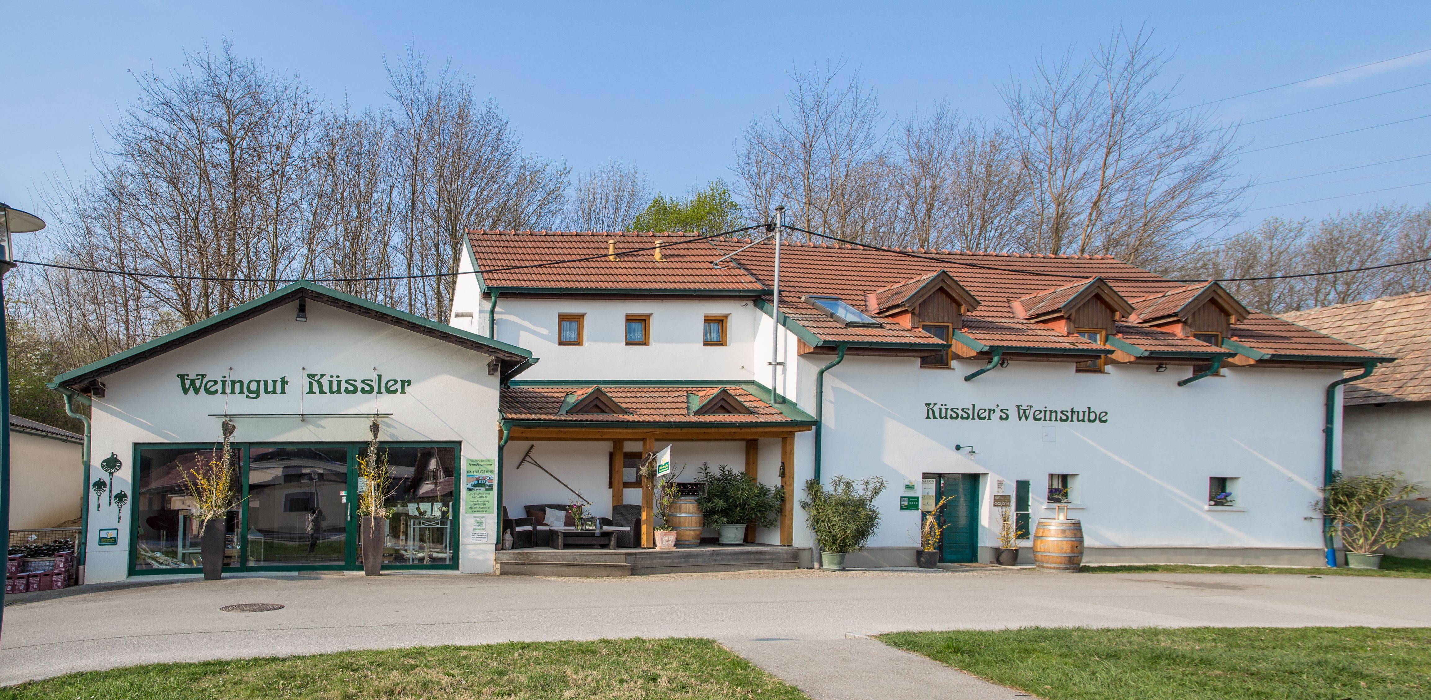 Weingut Küssler s vinárňou a terasou, obklopený stromami.