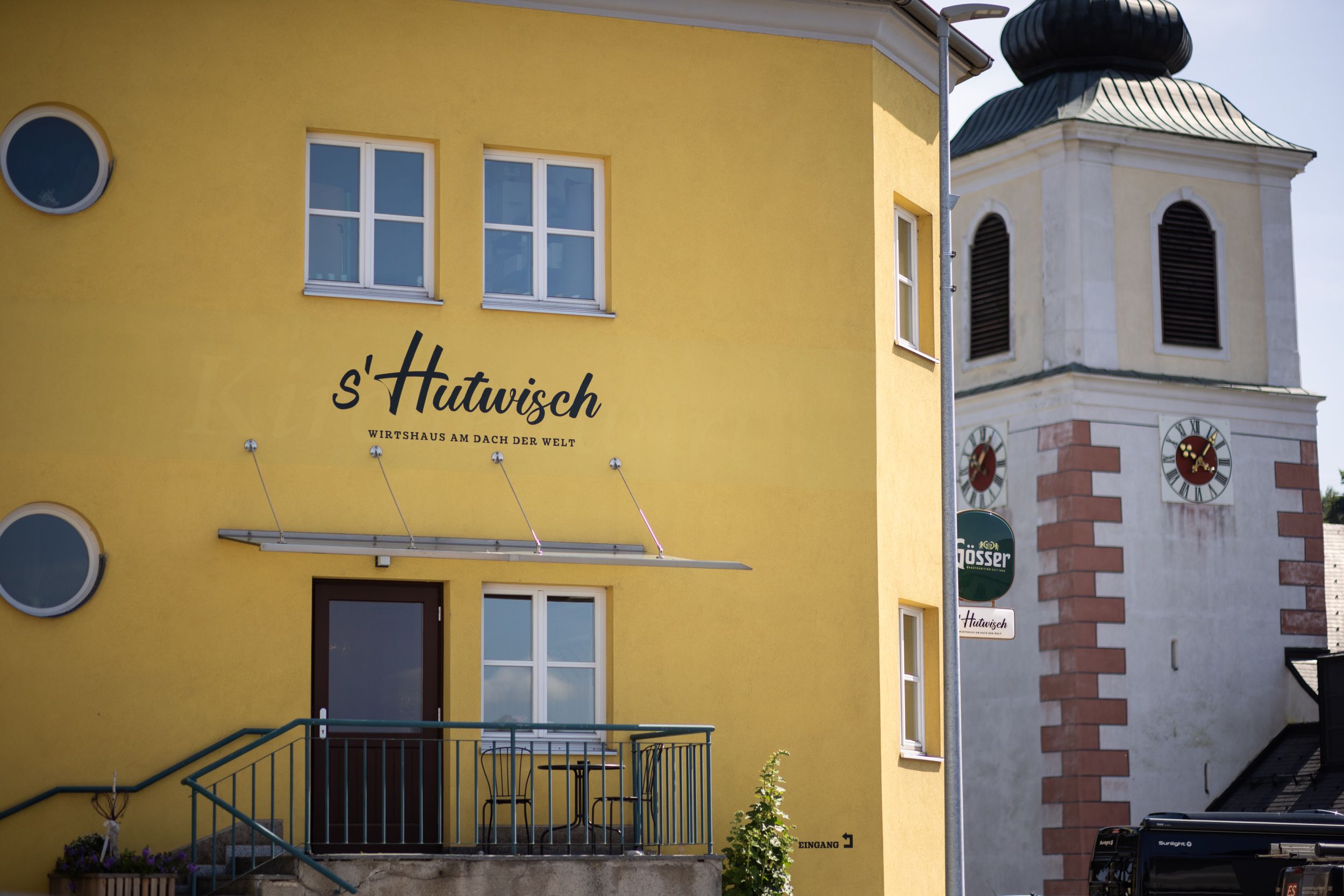 Žltá budova s označením "s'Hutwisch" vedľa kostolnej veže s hodinami.