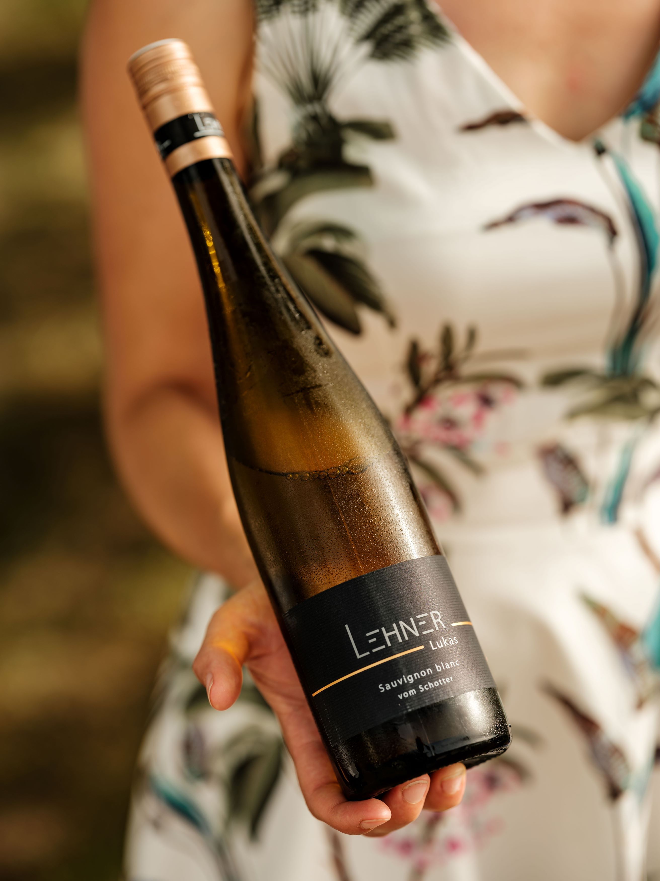 Jedna osoba drží fľašu vína s nápisom "Lehner Lukas Sauvignon blanc vom Schotter".