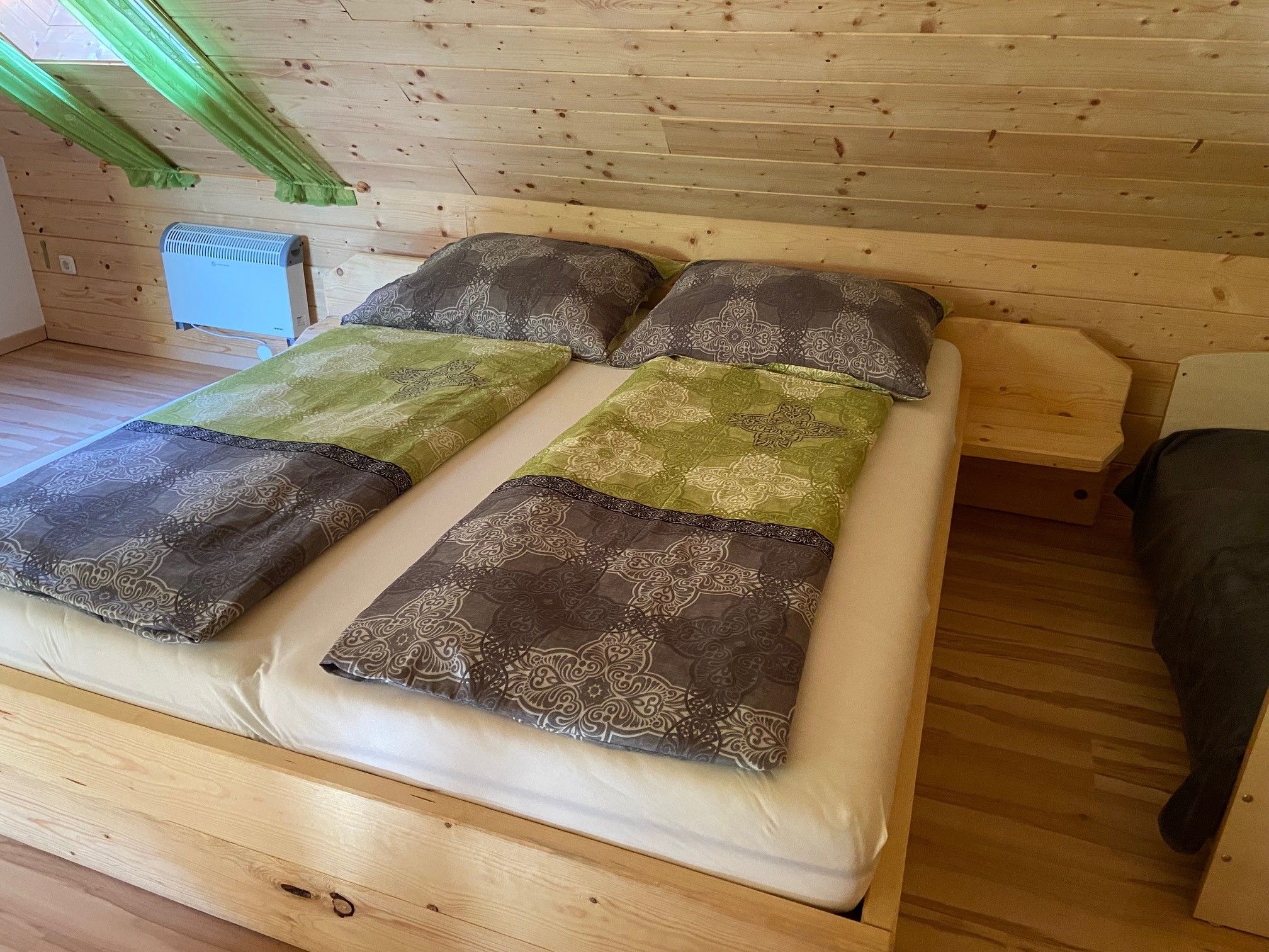 Manželská posteľ v izbe s dreveným obložením a zelenými závesmi.