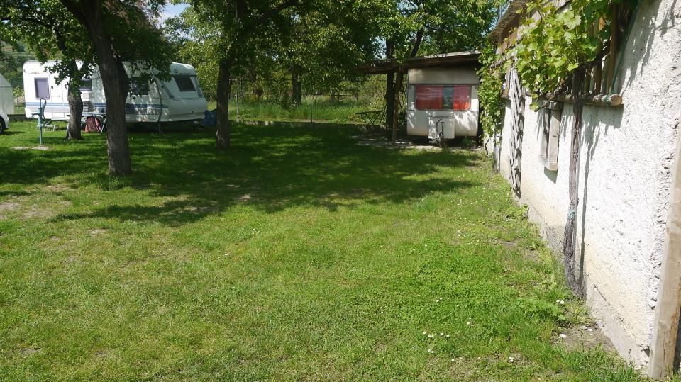 Kemp s karavanmi pod stromami, vedľa budovy s viničom.