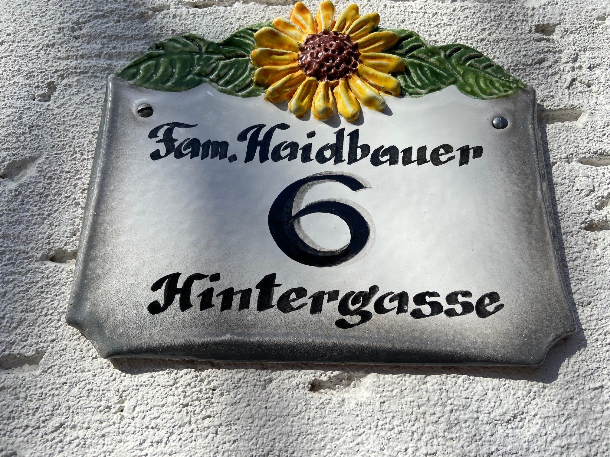 Tabuľka s číslom domu so slnečnicou a nápisom "Fam. Haidbauer 6 Hintergasse".