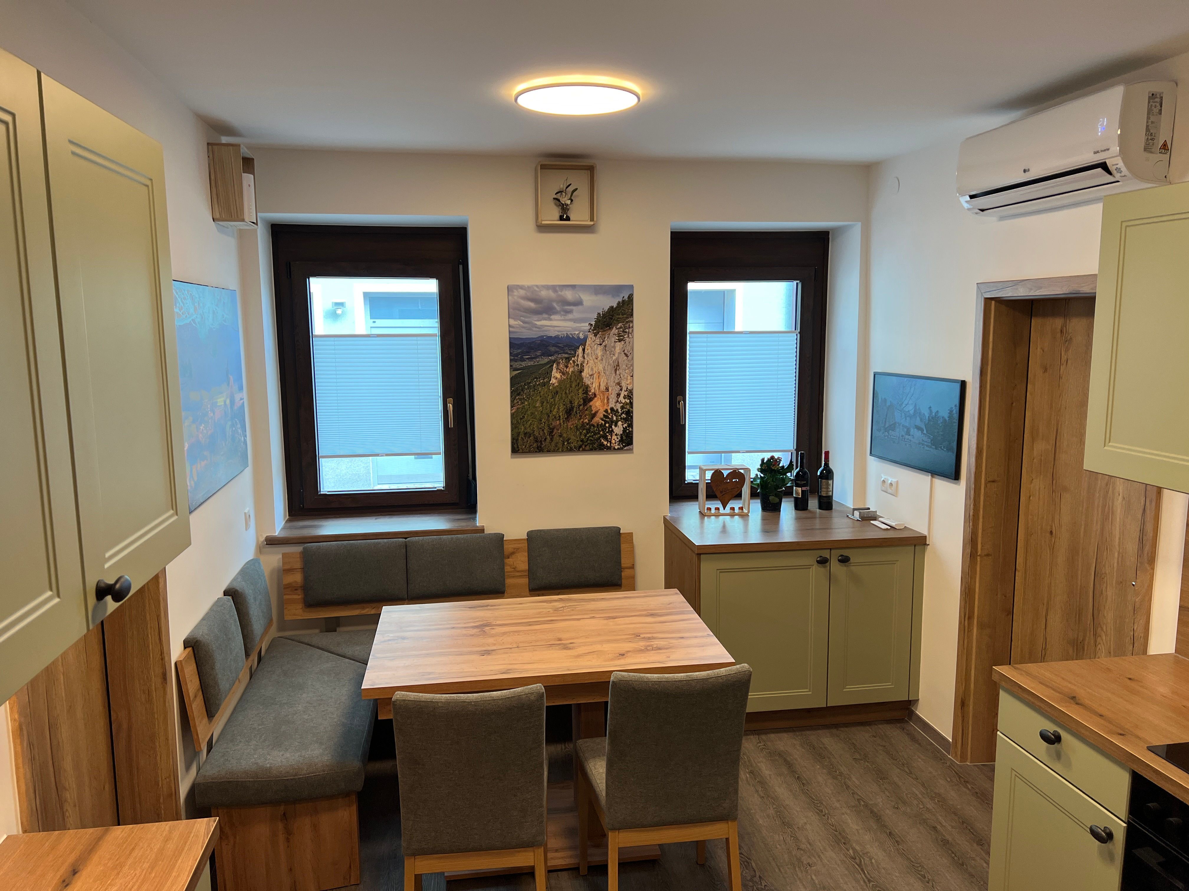 Moderná kuchyňa s dreveným nábytkom, jedálenským stolom a zelenými skrinkami.