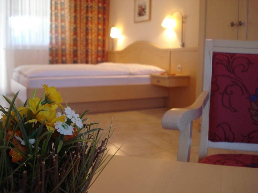 Útulná izba pre hostí s posteľou, stoličkou a stolíkom s kvetmi.