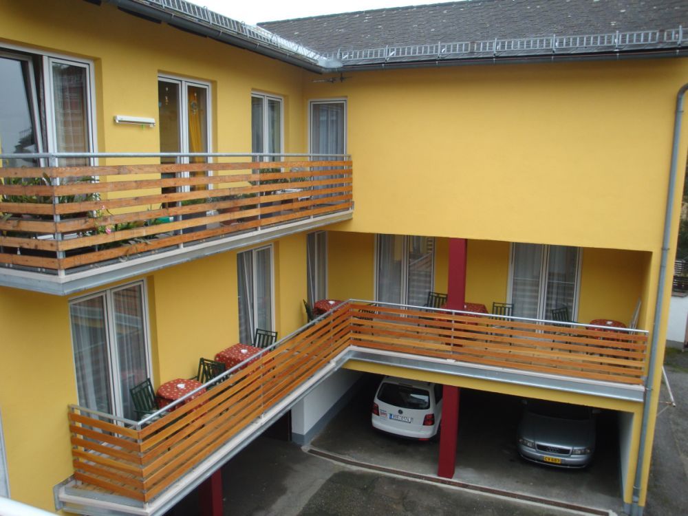 Žltá budova s balkónmi a zaparkovanými autami pod nimi.