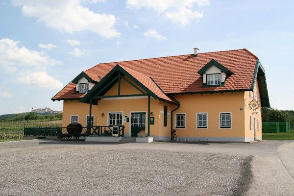 Žltý dom s červenou strechou a zelenými akcentmi, obklopený vidieckou krajinou.