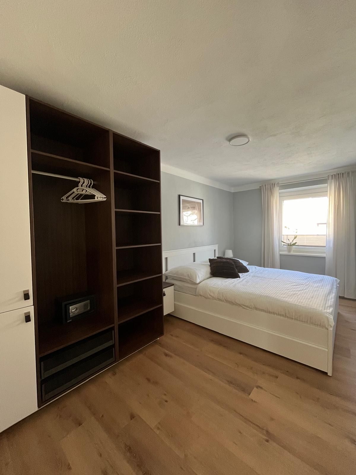 Moderná spálňa s manželskou posteľou, šatníkovou skriňou a oknom so závesmi.