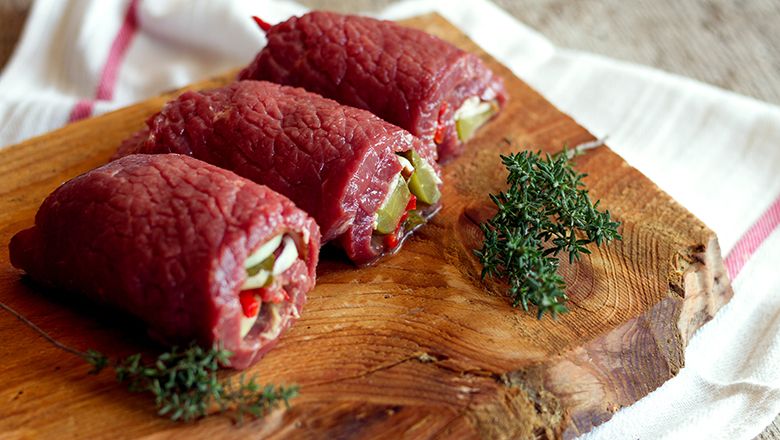 Tri plnené rolády zo surového hovädzieho mäsa na drevenej doske s vetvičkami tymiánu.
