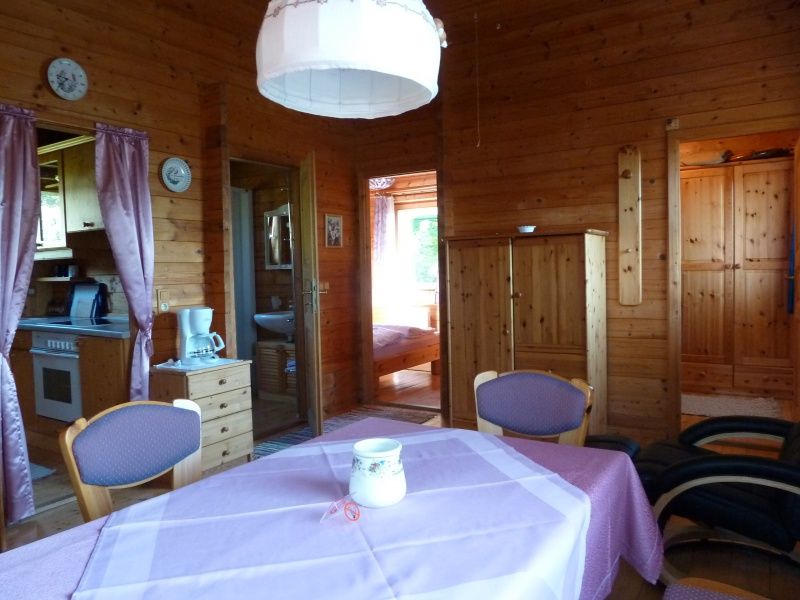 Pohľad do interiéru útulného rekreačného domu s drevenými stenami, jedálenským stolom a kuchynským kútom.