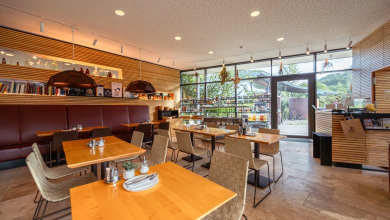 Pohľad do interiéru modernej reštaurácie s drevenými stolmi a veľkými oknami.