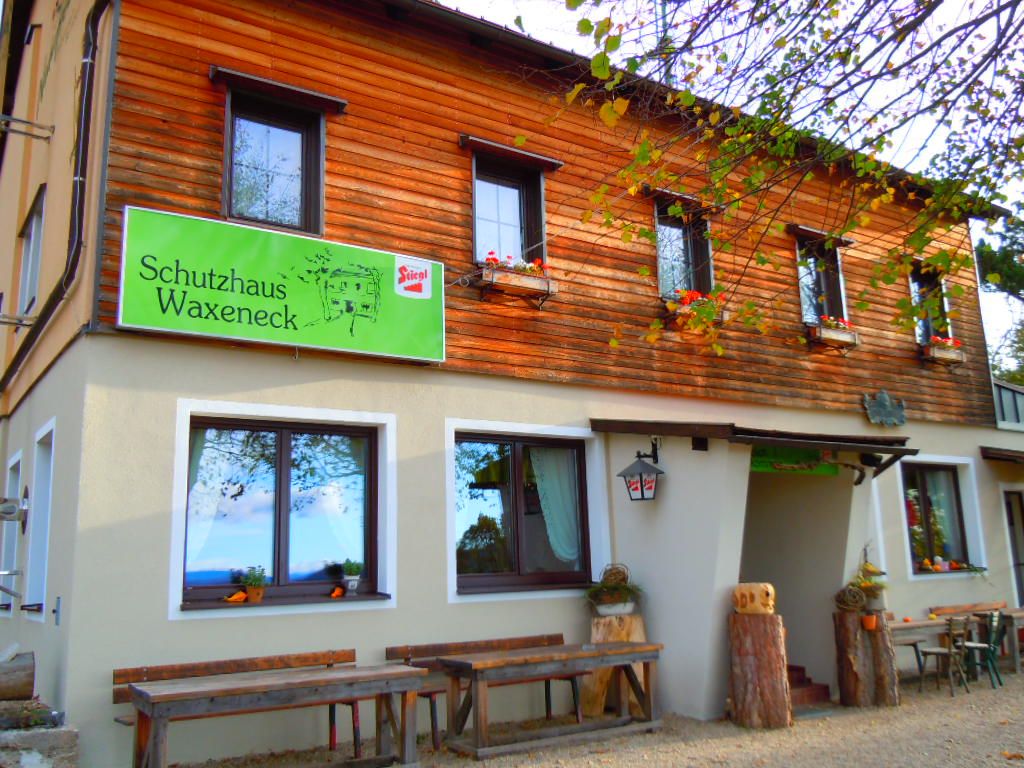 Vchod do prístrešku Waxeneck s drevenými stolmi a kvetinovými debničkami.