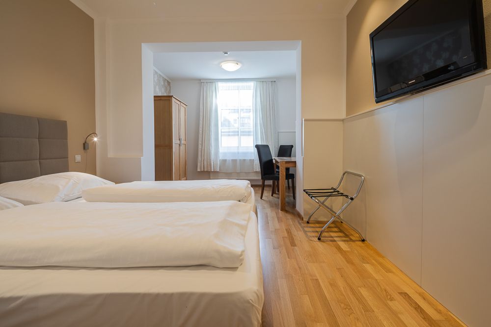 Hotelová izba s dvoma posteľami, televízorom, stolom a stoličkami.