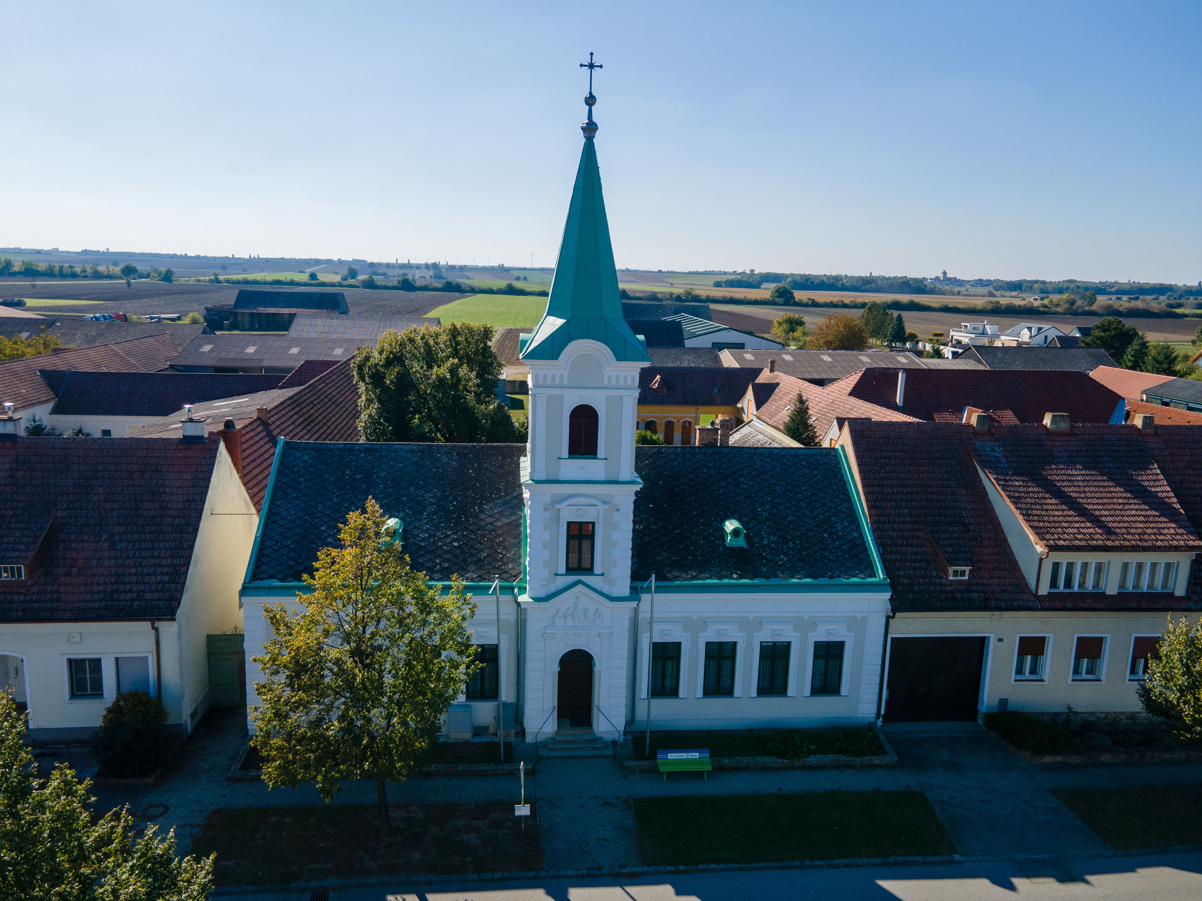 Kostol v obci Weiden an der March so zelenou vežou a krížom, obklopený domami a poľami.