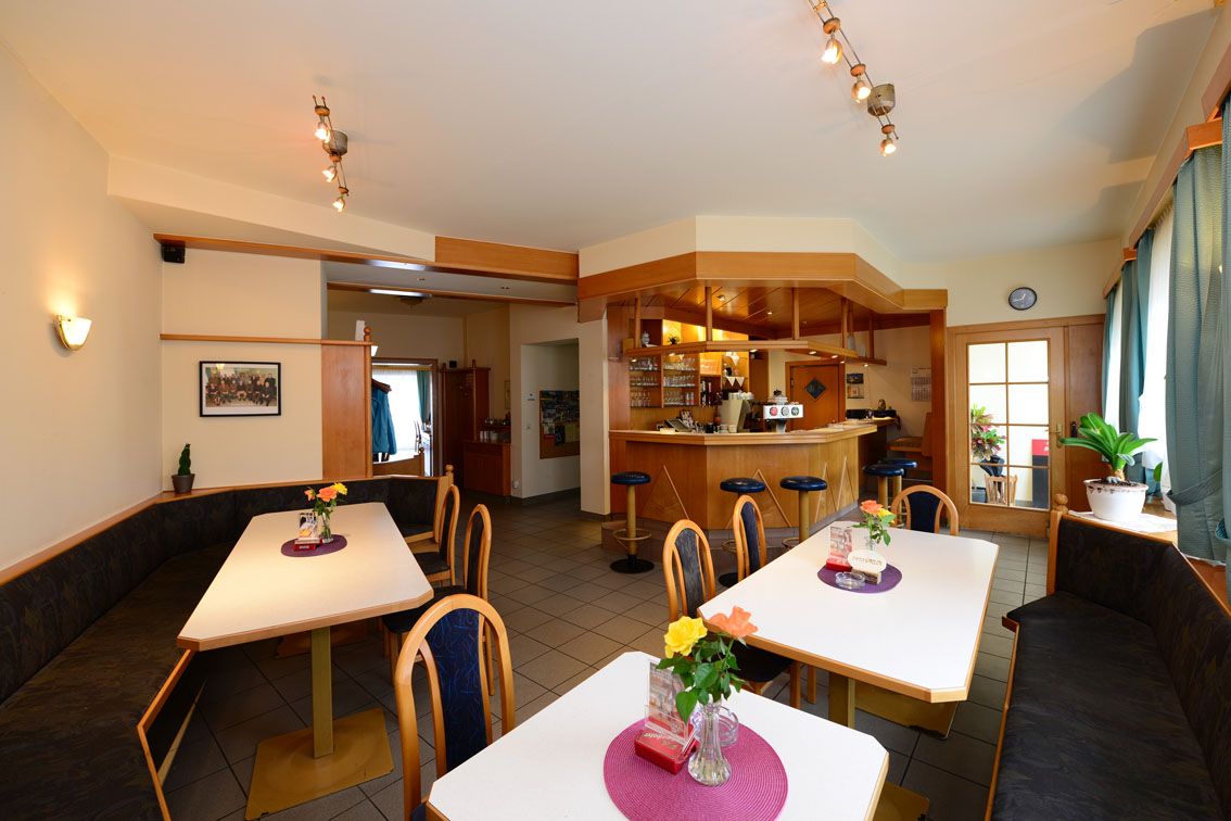 Pohľad do interiéru útulnej reštaurácie so stolmi, stoličkami a barom.