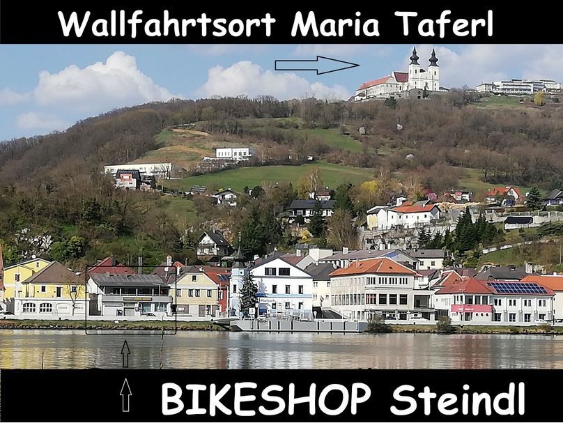 Pohľad na Maria Taferl s kostolom na kopci, pod obcou a nápisom na predajňu bicyklov Steindl.