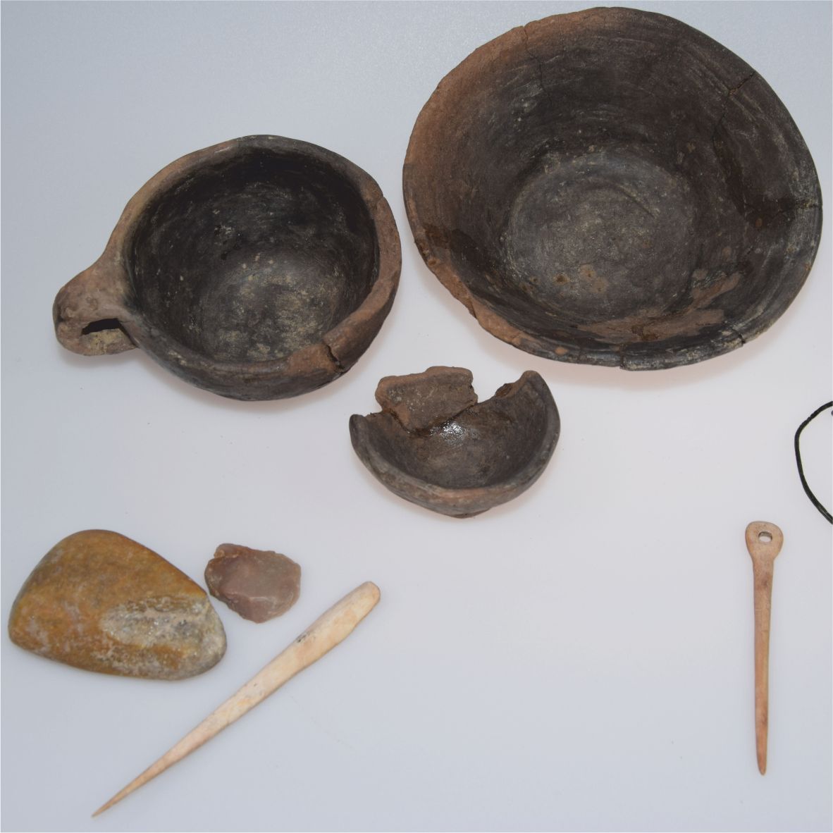 Prehistorické artefakty ako misky, nástroje a kamene na bielom pozadí.