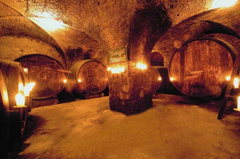 Historická vínna pivnica s veľkými drevenými sudmi a svetlom sviečok.