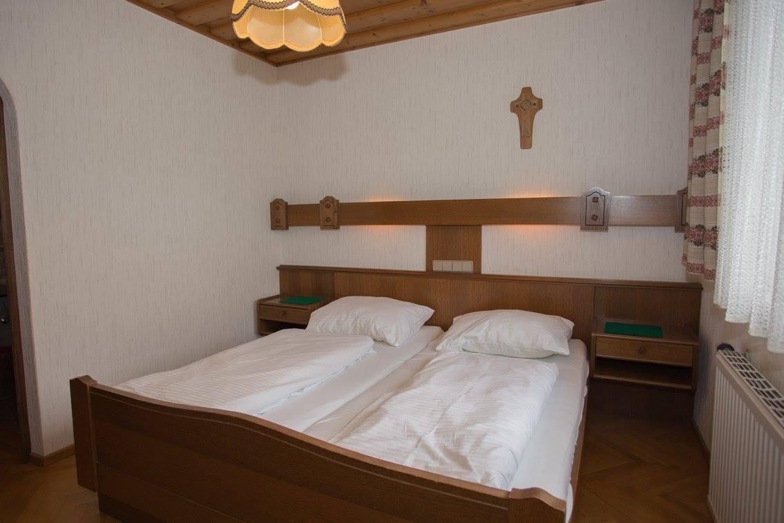 Tradičná dvojlôžková izba s dreveným nábytkom, dvoma posteľami, krížom na stene a lampou na strope.