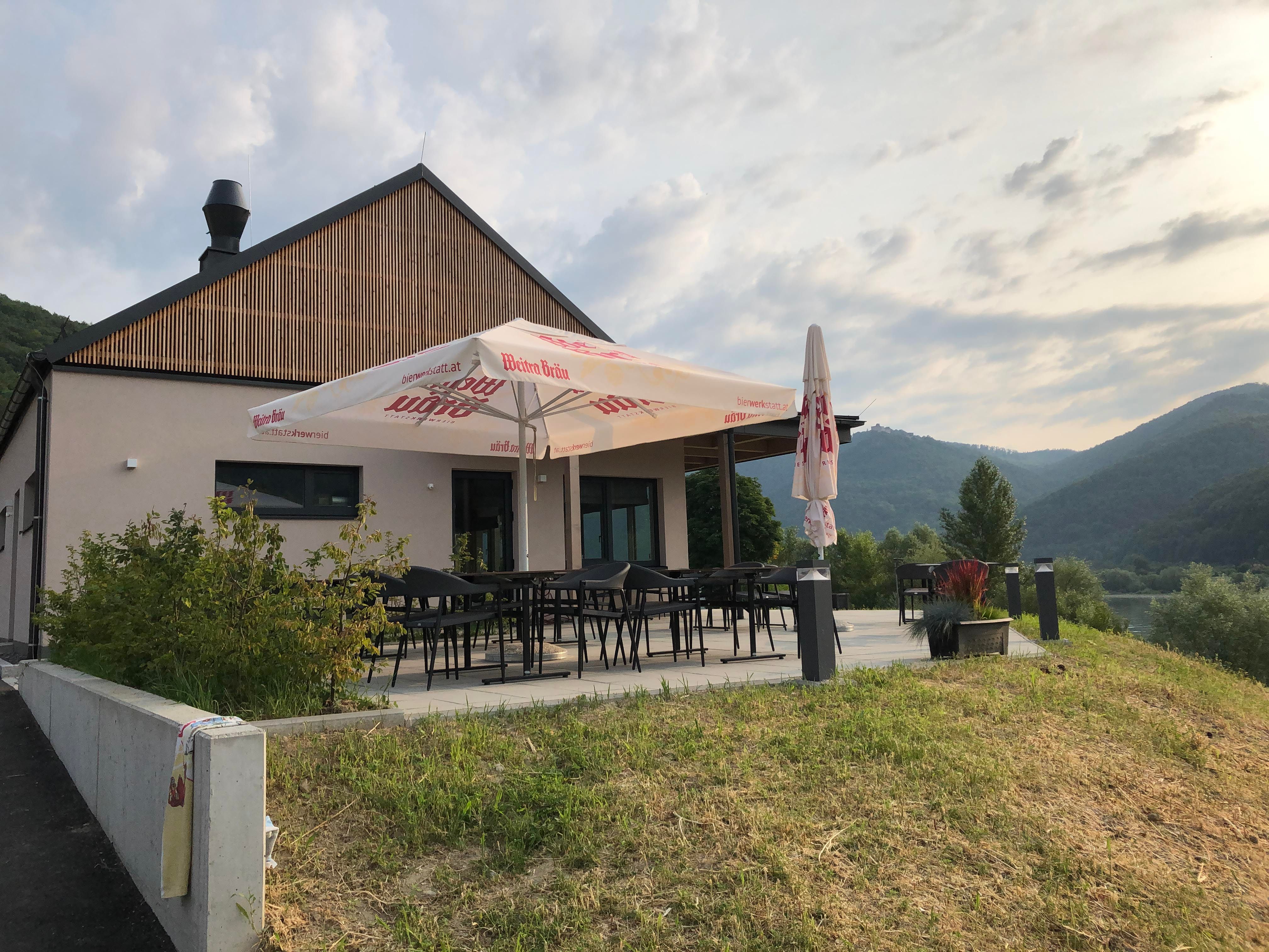 Moderná terasa so slnečníkom, obklopená zelenou krajinou a kopcami.