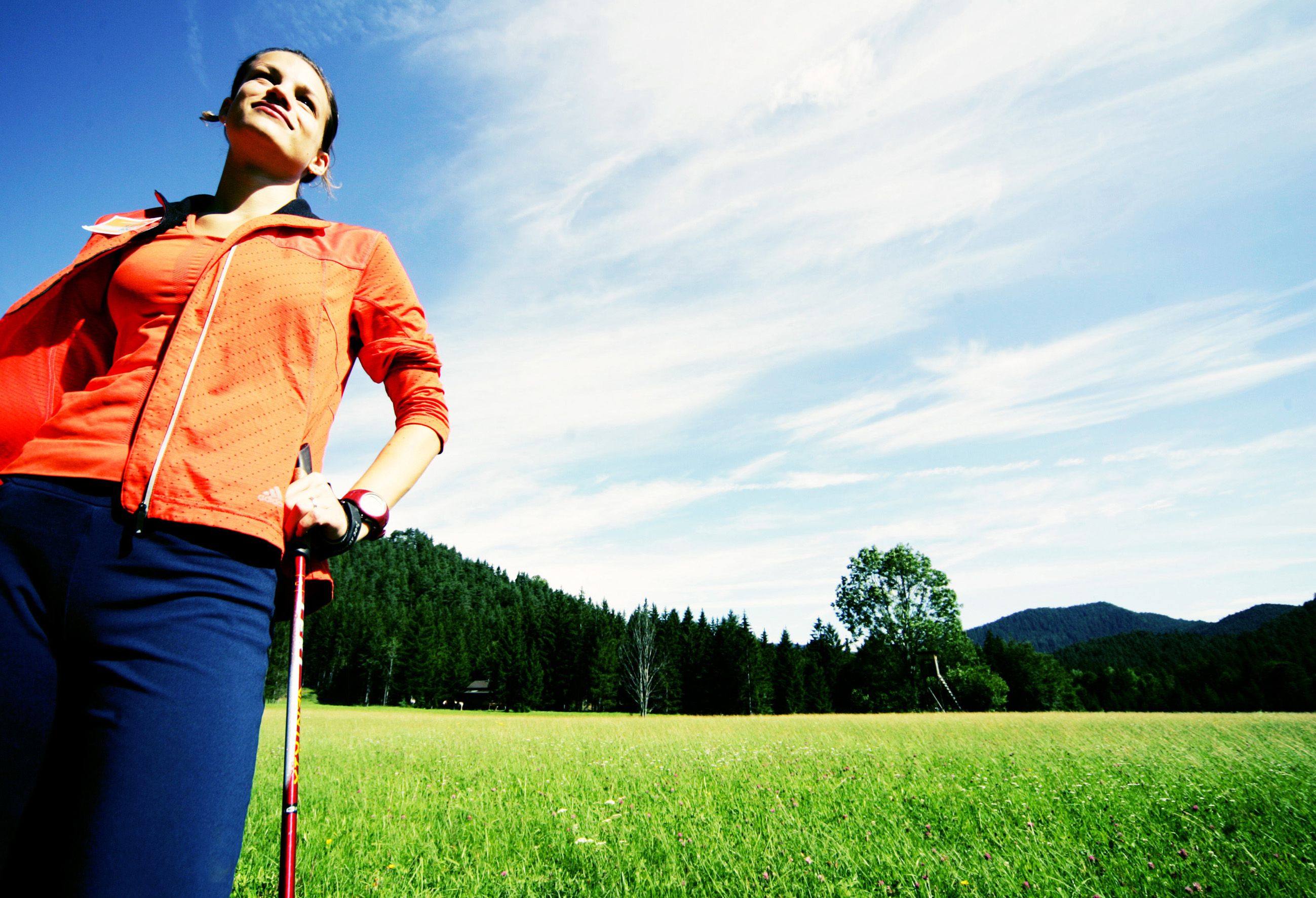Žena v športovom oblečení s paličkami na nordic walking na lúke pred lesom.