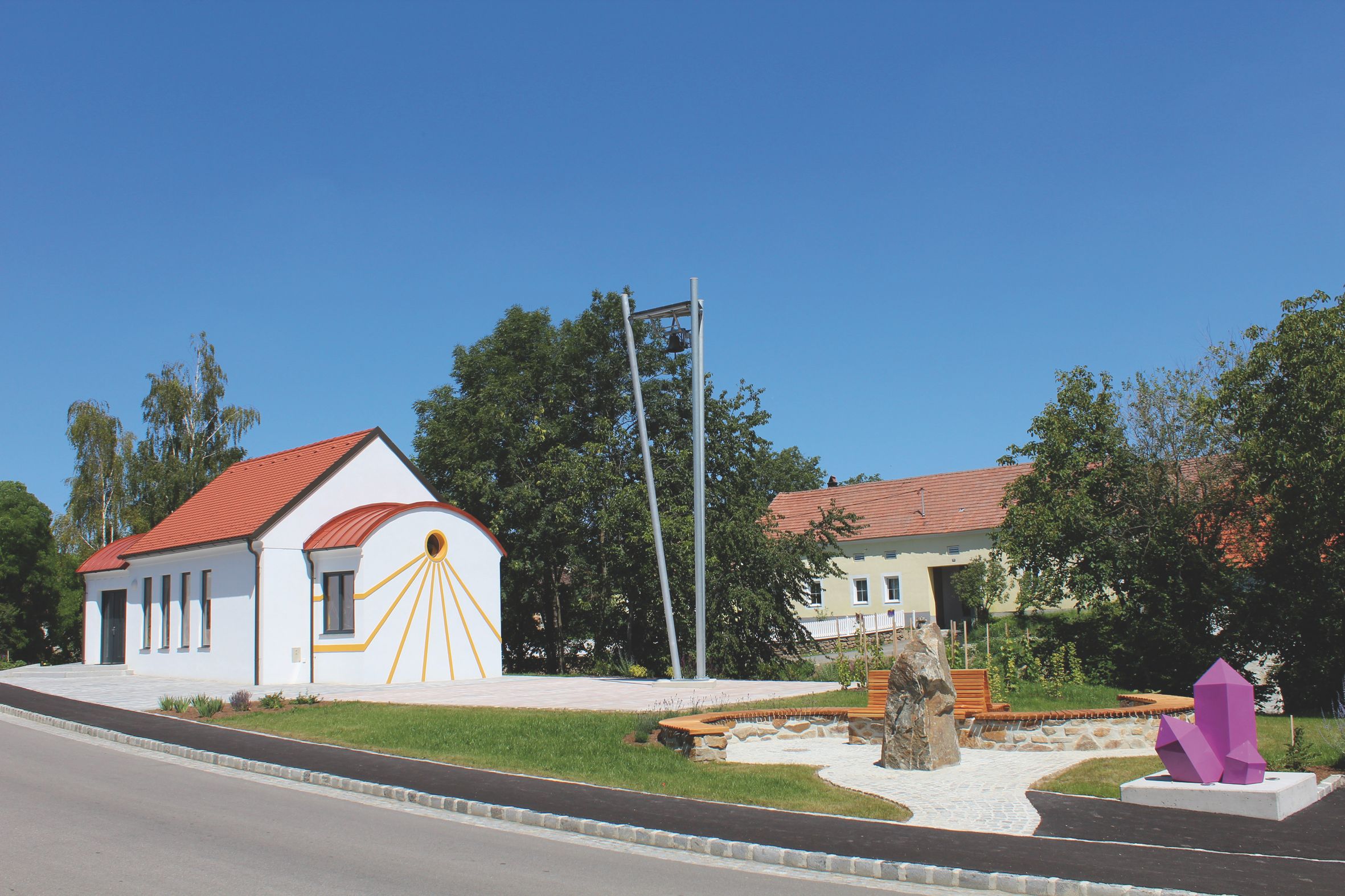 Biela kaplnka s červenou strechou a ametystovou sochou v popredí.