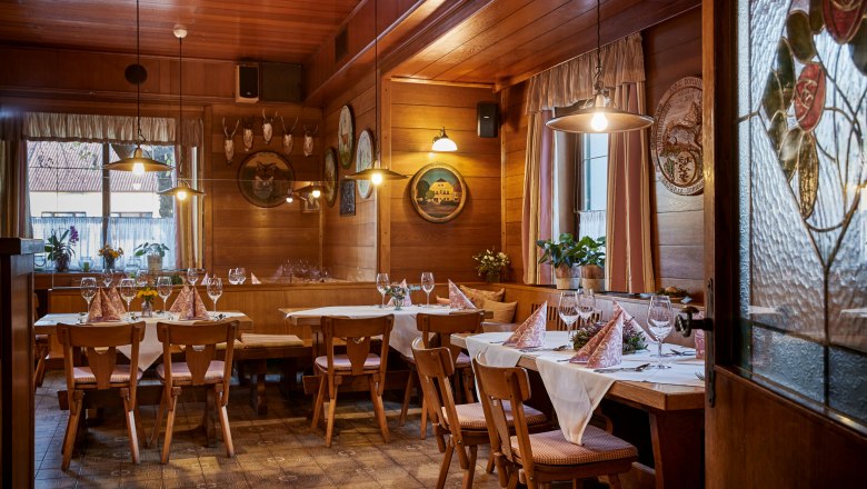 Útulná, drevom obložená krčma s prestretými stolmi, stoličkami a dekoratívnymi prvkami na stenách.