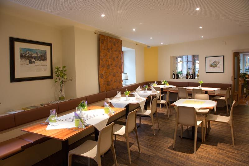 Moderná jedáleň s prestretými stolmi, stoličkami a dekoráciami. Na stenách visia obrazy a na parapete sú fľaše s vínom.