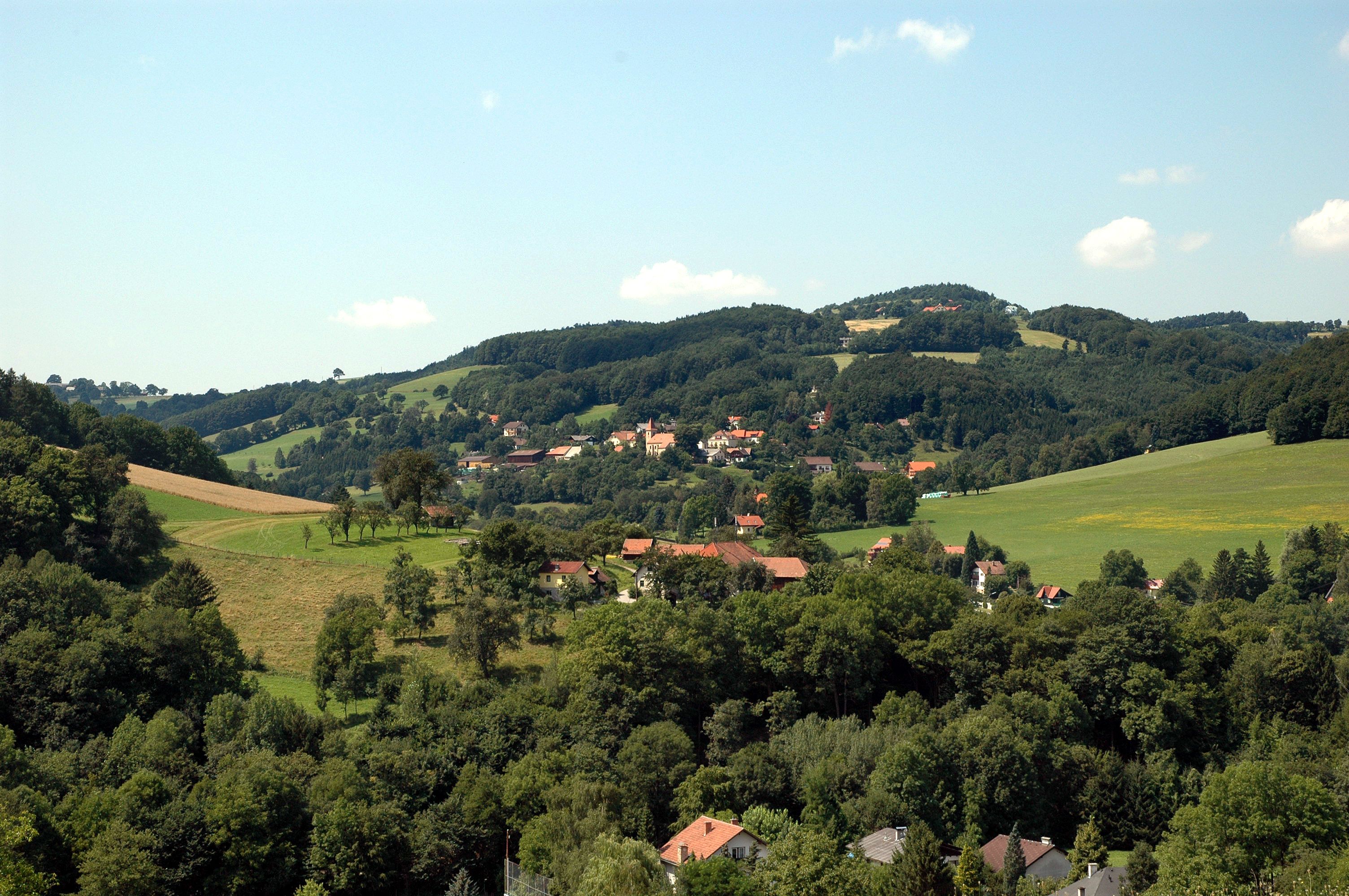 Krajina s kopcami, lesmi a dedinou v pozadí.