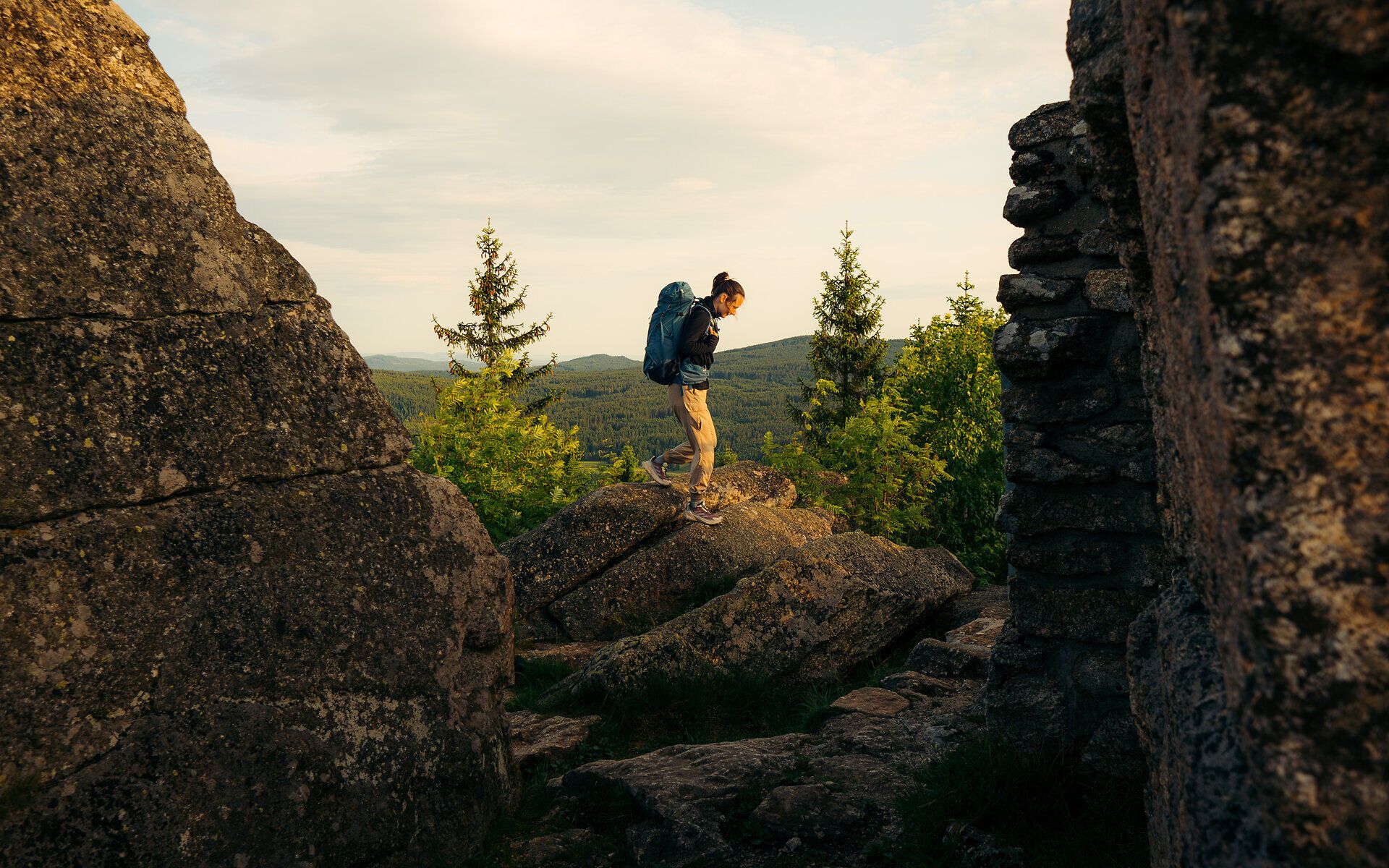 Eine Frau stehen zwischen imposanten Felsformationen und geht gerade weiter, hinter ihr die Weite des Waldviertels mit der Waldlandschaft 