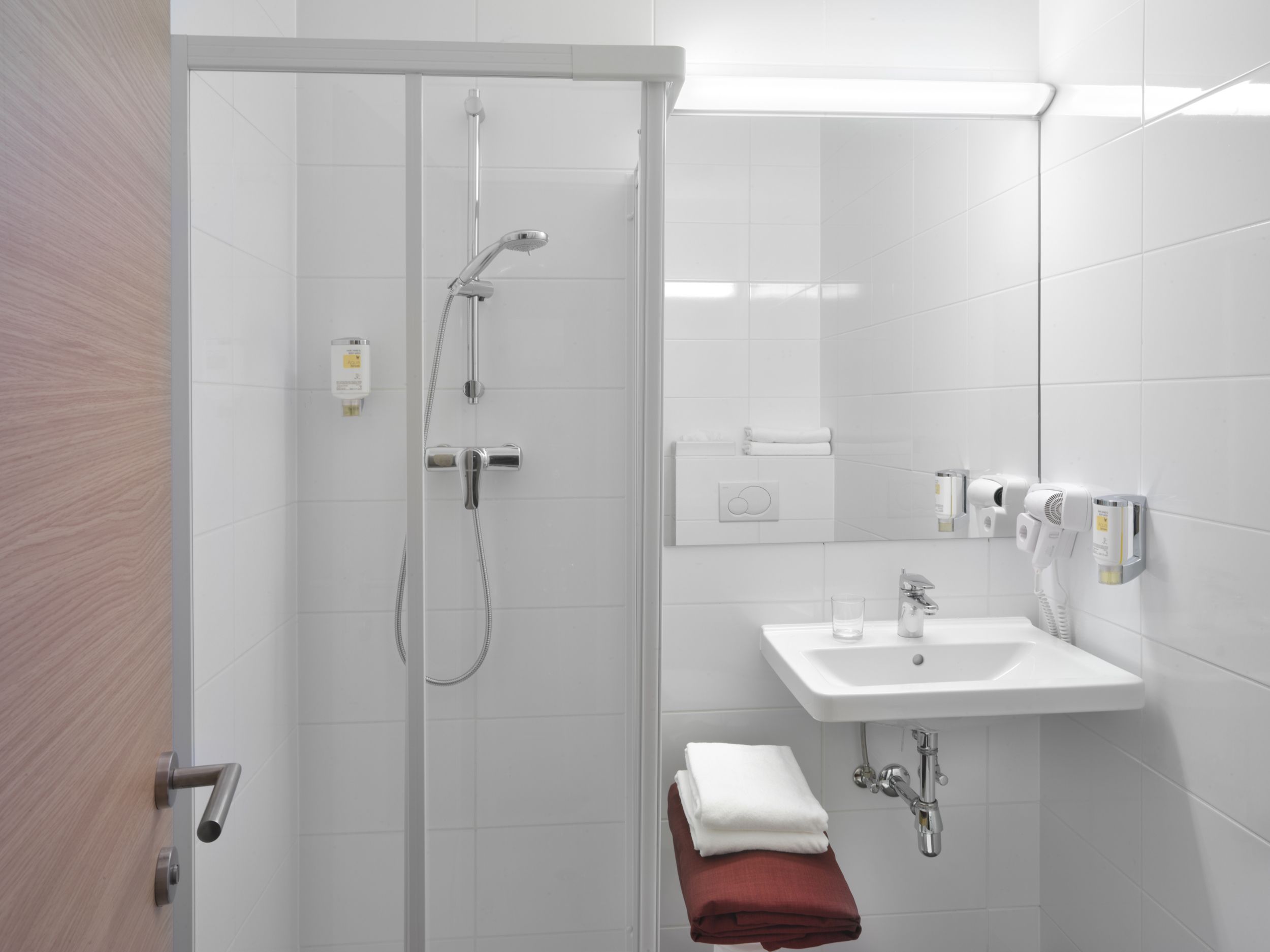 Moderná hotelová kúpeľňa so sprchovacím kútom, umývadlom a uterákmi.