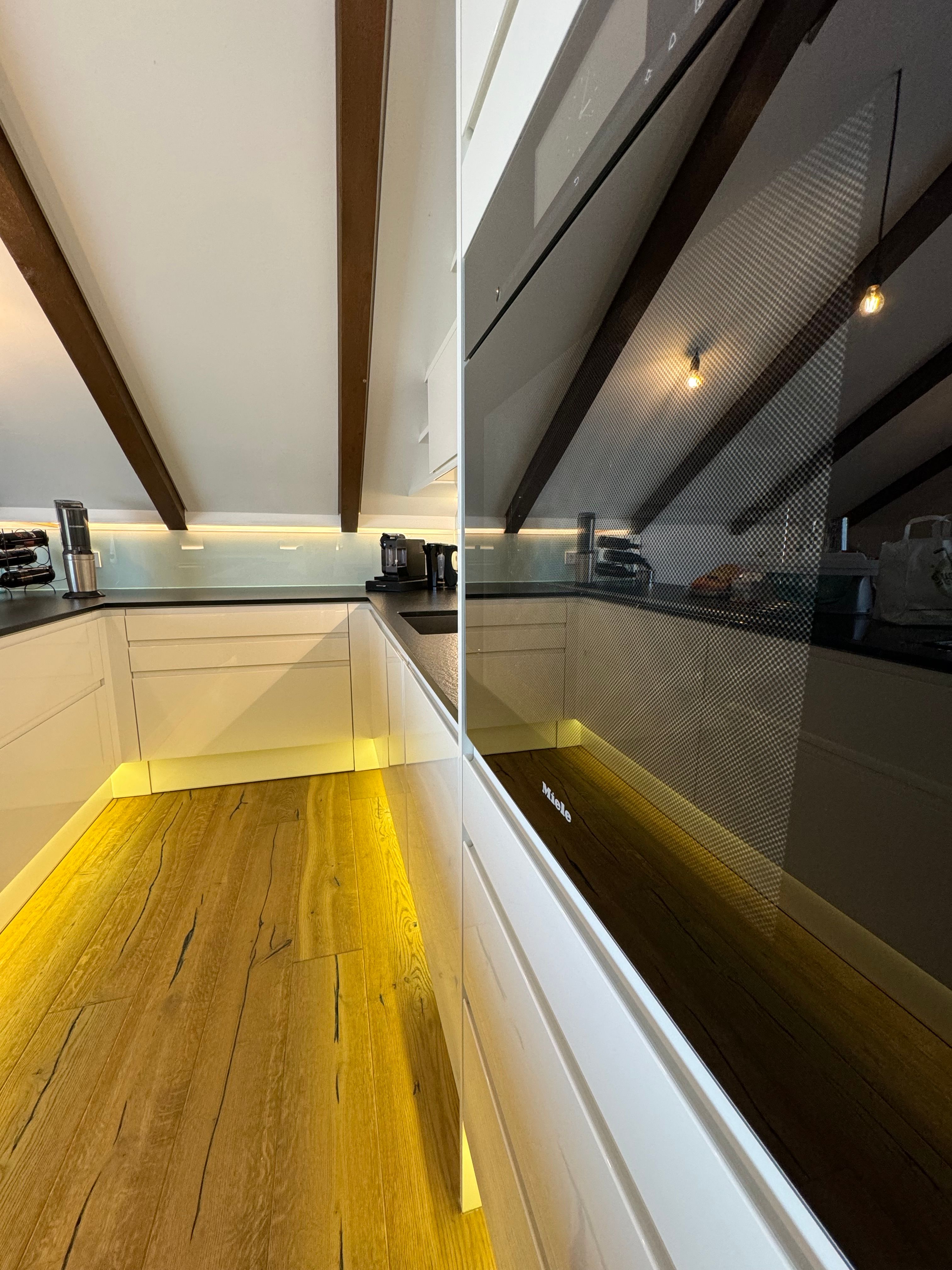 Moderná kuchyňa s drevenou podlahou, bielymi skrinkami a vstavanou rúrou.