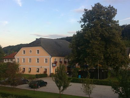 Pohľad na žltý hostinec s veľkým stromom a parkoviskom.