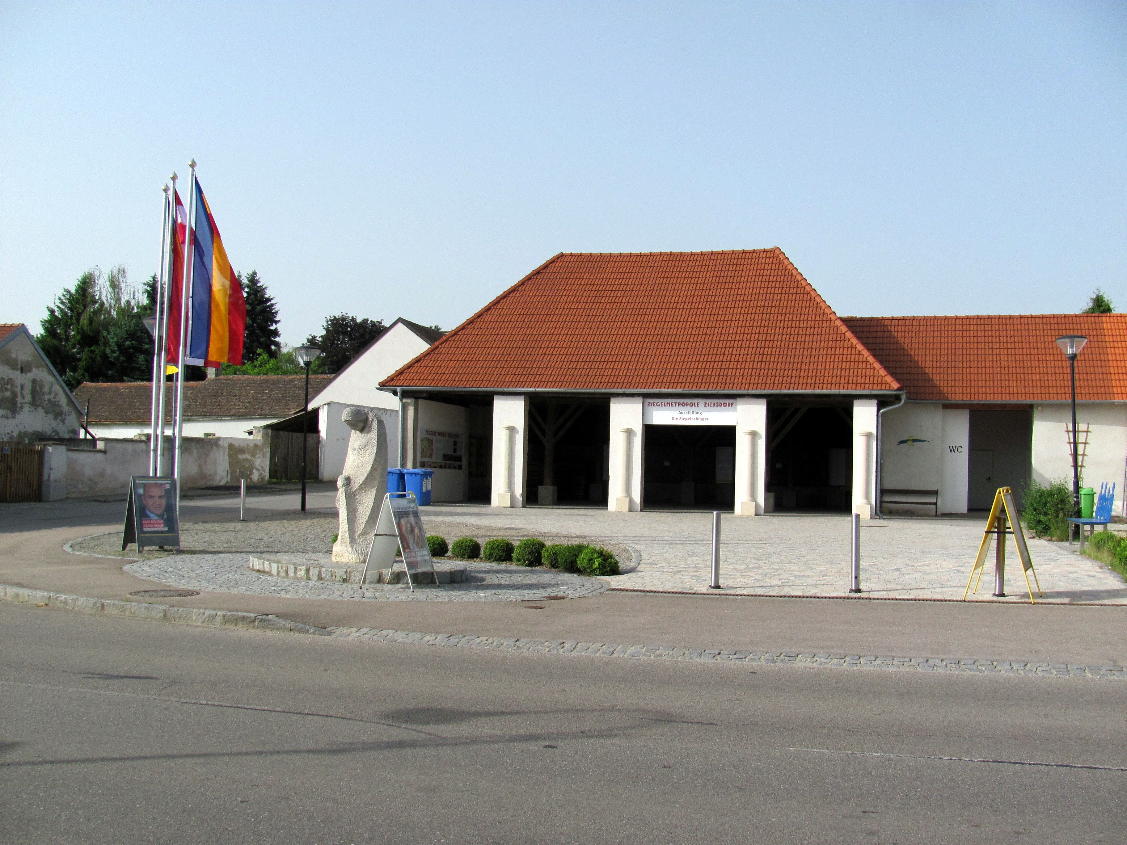 Pohľad na tehlové múzeum v Ziersdorfe z exteriéru s červenými strešnými škridlami a vlajkami.