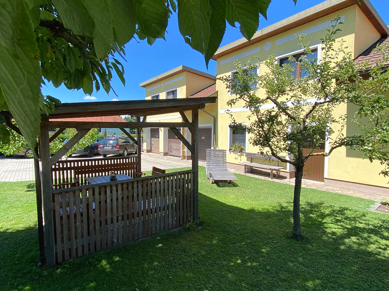 Záhrada s pavilónom, žltým domom a autom v pozadí.