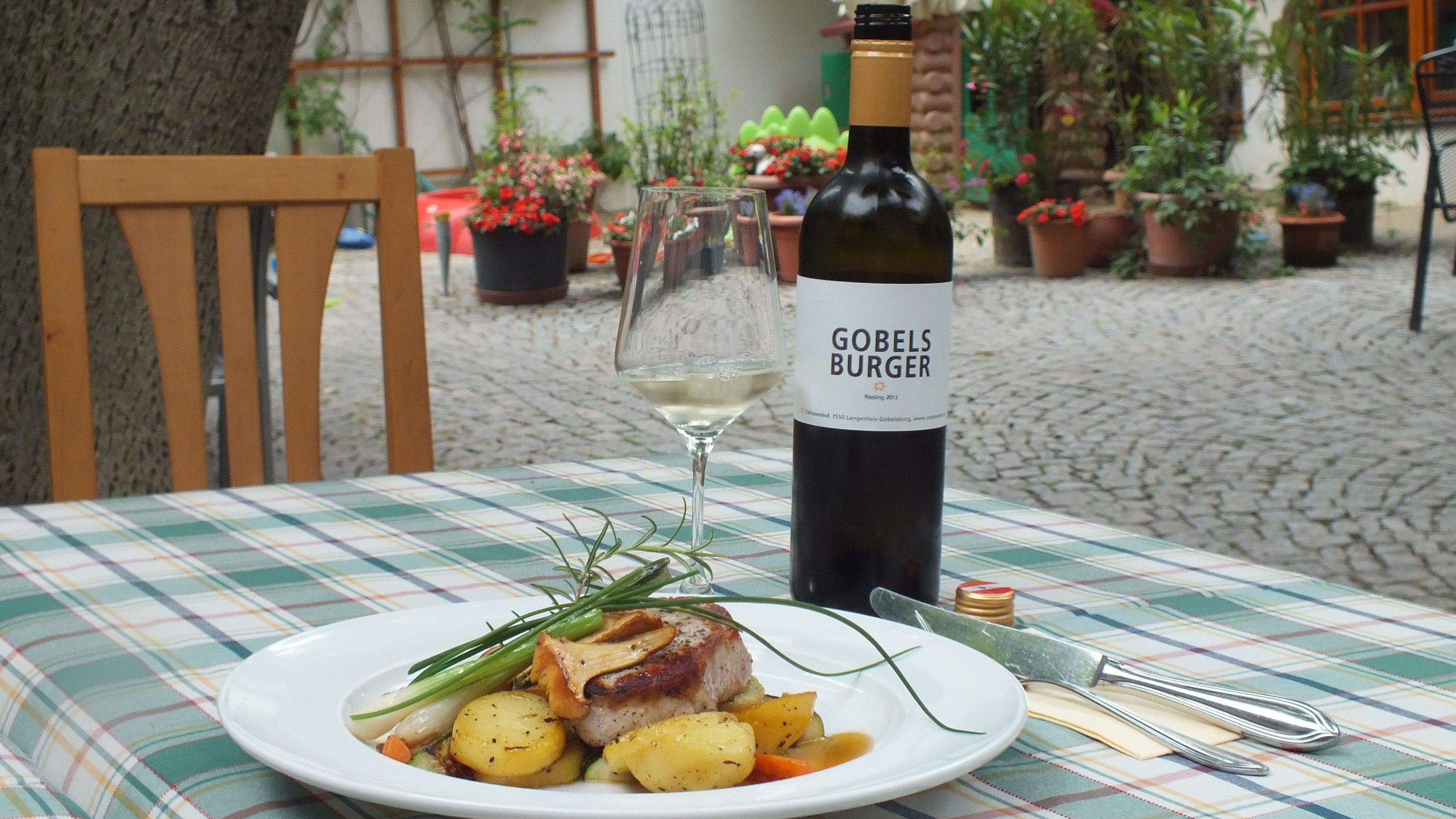 Na vonkajšom stole tanier s mäsom a zemiakmi, vedľa fľaša vína a pohár.