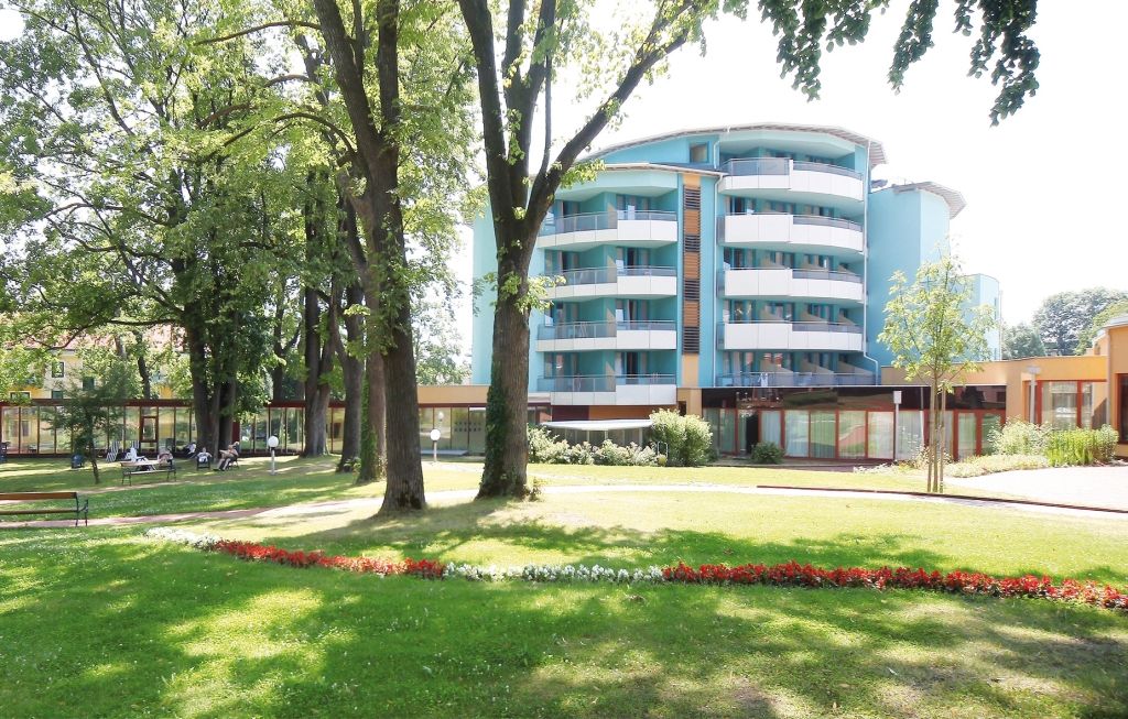 Moderná budova s balkónmi a záhradou v popredí.