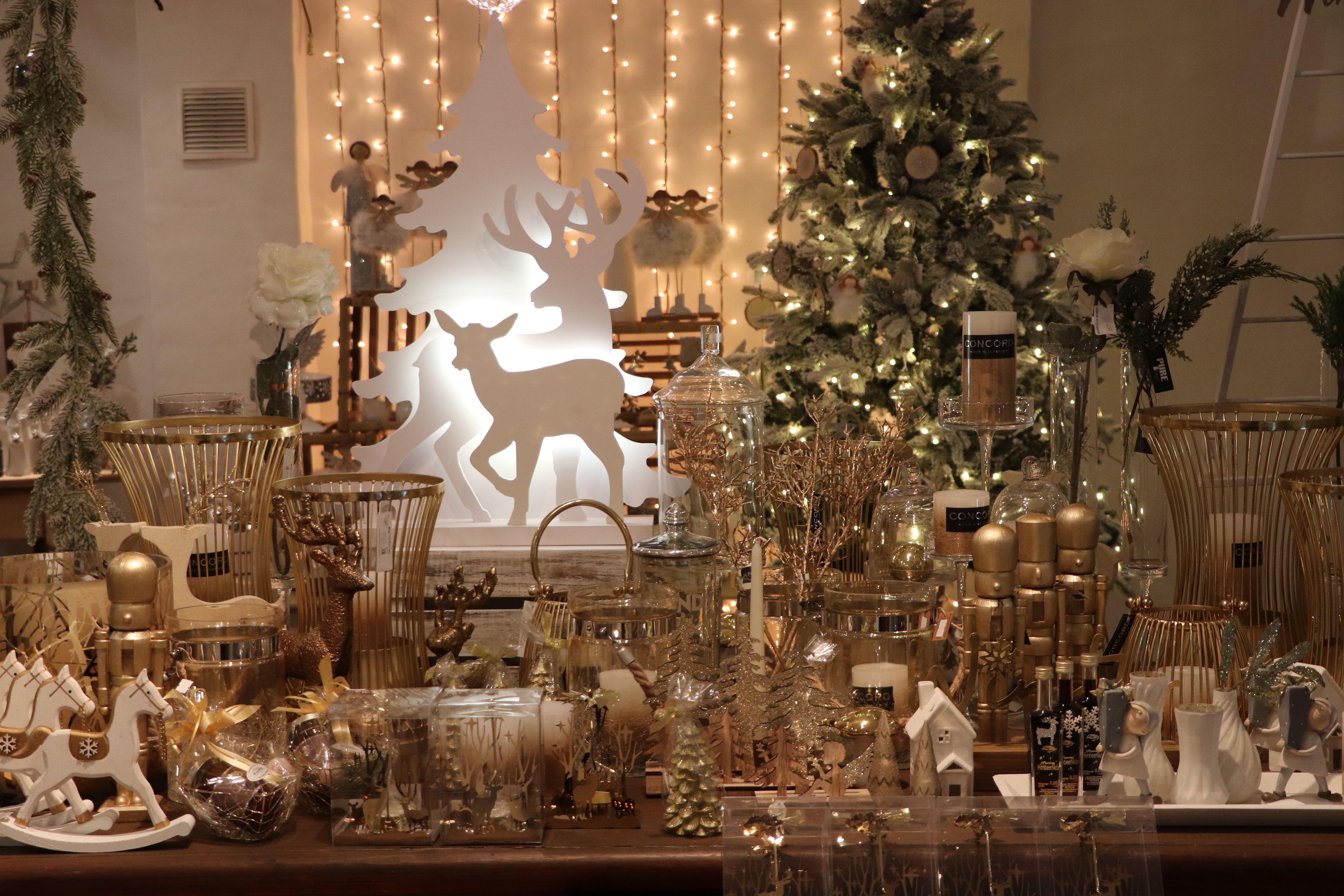 Vianočné ozdoby so zlatými a bielymi prvkami vrátane sviečok, sobov a vianočného stromčeka v pozadí.