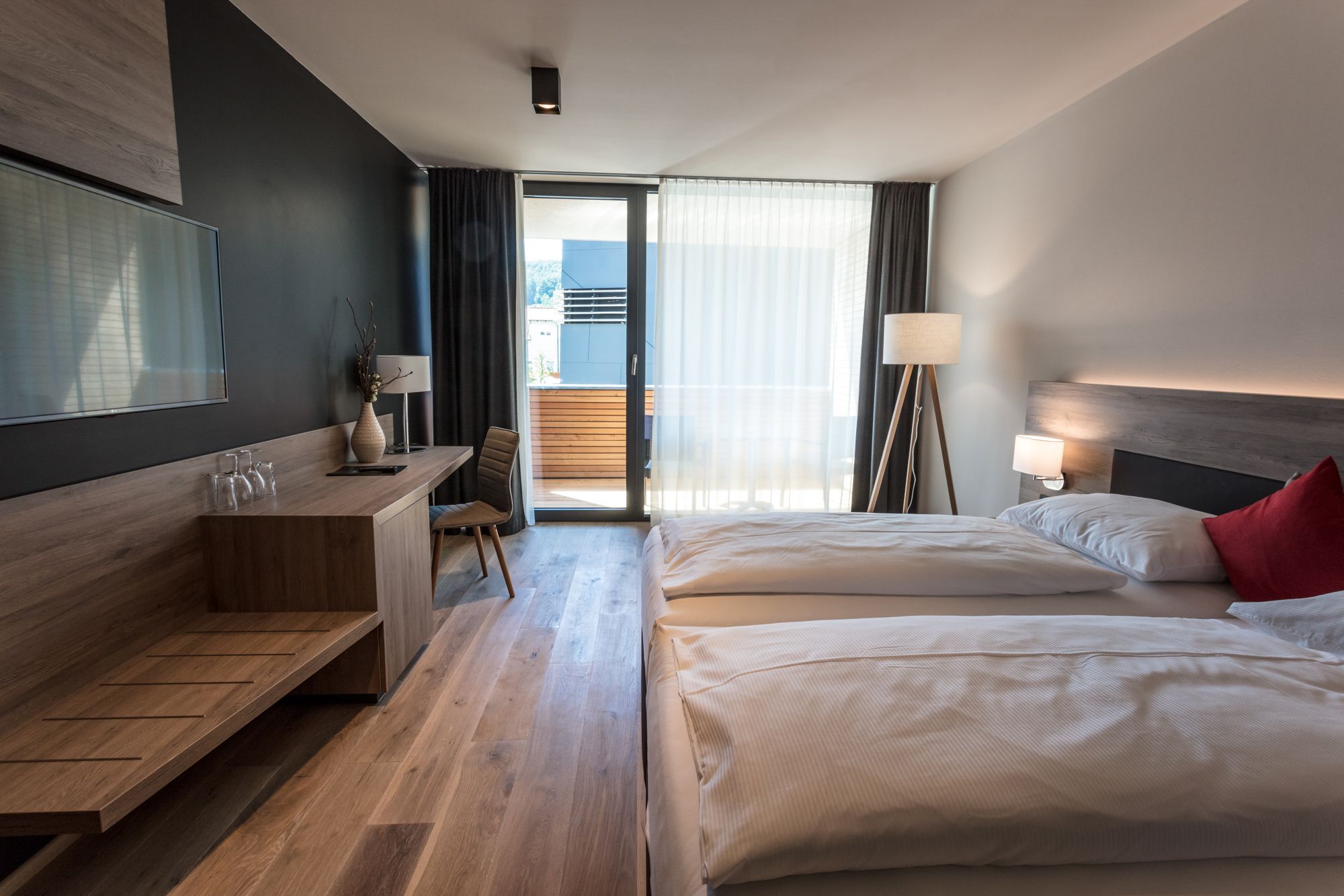 Moderná hotelová izba s dvoma posteľami, písacím stolom a balkónom.